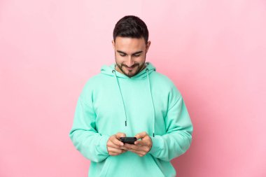 Pembe arka planda izole edilmiş genç beyaz adam cep telefonuyla bir mesaj gönderiyor.