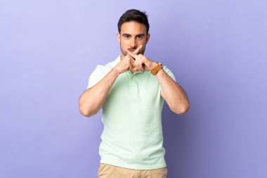 Mor arka planda izole edilmiş genç yakışıklı bir adam sessizlik işareti gösteriyor.
