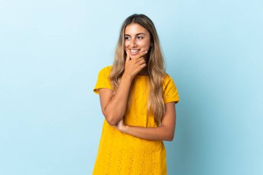 İzole edilmiş mavi arka planda genç bir İspanyol kadın yana bakıyor ve gülümsüyor.