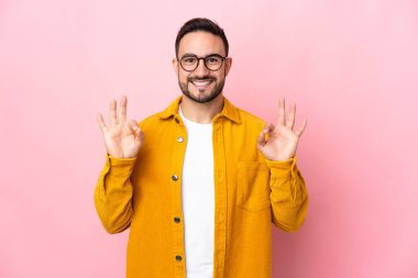 Pembe arka planda izole edilmiş beyaz, yakışıklı genç bir adam iki eliyle tamam işareti gösteriyor.
