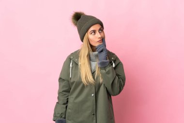 Kış şapkalı genç kadın pembe arka planda izole edilmiş gülümserken yukarı bakıyor.