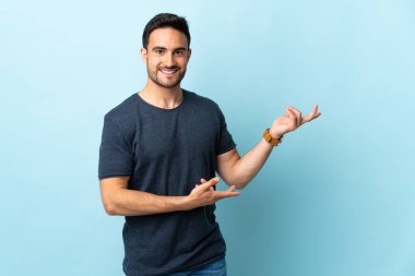 Soyutlanmış arka planda genç yakışıklı adam, davet edilmek için ellerini yana uzatıyor.