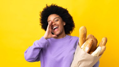 Genç Afrikalı Amerikalı bir kadın sarı arka planda izole edilmiş bir şey alıyor ve ağzı açık bağırıyor.