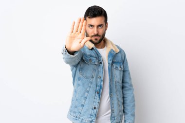 Beyaz arka planda sakallı yakışıklı genç adam dur hareketi yapıyor.