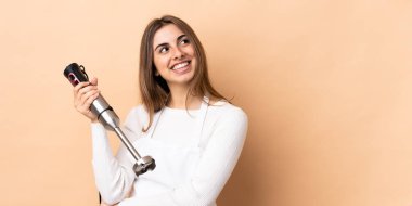 İzole edilmiş arkaplanda el blenderi kullanan bir kadın harika bir fikre işaret ediyor.