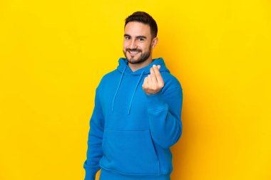 Sarı arka planda izole genç beyaz yakışıklı adam para hareketi yapıyor.