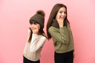 Pembe arka planda izole edilmiş kışlık giysiler giyen küçük kardeşler ön tarafa bakıyor.