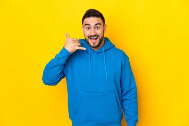 Sarı arka planda izole edilmiş beyaz, yakışıklı genç bir adam telefon jesti yapıyor. Bana geri dönüş işareti ver.