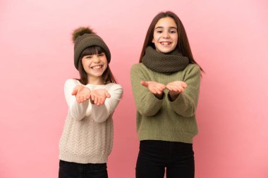 Küçük kız kardeşler pembe arka planda izole edilmiş kışlık giysiler giyiyorlar.