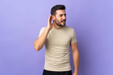 Sakallı ve sakallı genç bir adam. Kulağına elini sürerek bir şeyler dinliyor.