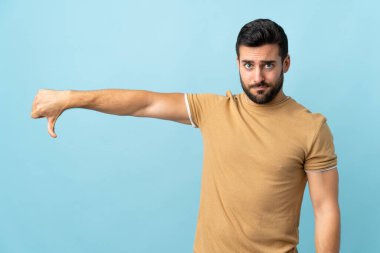Sakallı, soyutlanmış, genç ve yakışıklı bir adam, olumsuz bir ifadeyle baş parmağını gösteriyor.