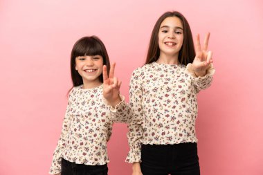 Pembe arka planda izole edilmiş küçük kız kardeşler gülümsüyor ve zafer işareti gösteriyor.