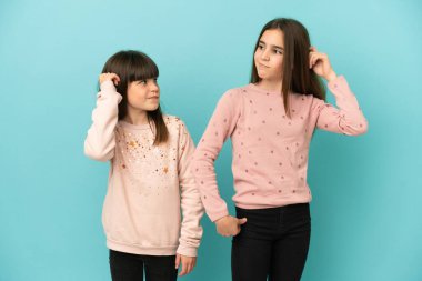 Küçük kız kardeşler mavi arka planda izole edilmiş kafaları kaşınırken şüpheleri olan kızlar.