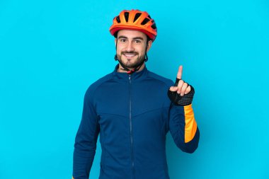 Genç bisikletçi mavi arka planda izole edilmiş ve en iyinin işareti olarak parmağını kaldırıyor.
