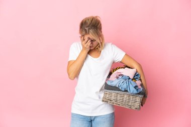 Pembe arka planda izole edilmiş, yorgun ve hasta bir ifadeyle bir çamaşır sepeti tutan genç Rus kadın.