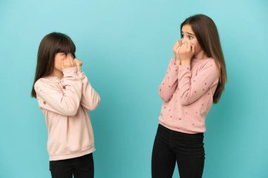 Mavi arka planda izole edilmiş küçük kız kardeşler biraz gergin ve korkaktır.