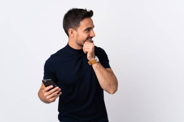 Beyaz arka planda izole edilmiş bir şekilde cep telefonu kullanan genç beyaz bir adam bir fikir üretiyor ve bakıyor.