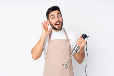 Beyaz arkaplanda izole edilmiş el blenderi kullanan bir adam bir şeyler dinliyor.