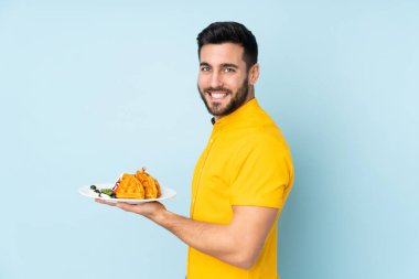 Mavi arka planda izole edilmiş waffle 'lar tutan beyaz adam çok gülümsüyor.