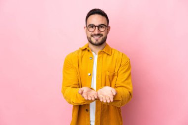 Beyaz tenli yakışıklı, pembe arka planda izole edilmiş. Avucunun içinde hayali bir ilan tutuyor.