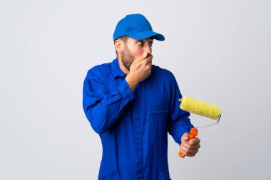 Boyacı beyaz arka planda izole edilmiş bir boya silindiri tutuyor. Ağzı kapatıyor ve yan tarafa bakıyor.