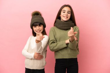 Pembe arka planda izole edilmiş kışlık giysiler giyen küçük kız kardeşler bizimle gelmek için davet ediyorlar. Gelmene sevindim.