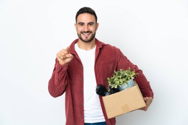 Young caucasian man making a move while picking up a box full of things isolated on white background surprised and pointing front