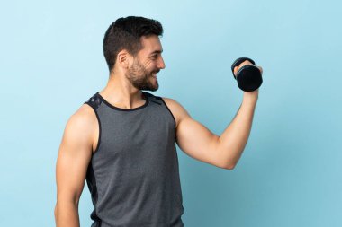 Sakallı genç sporcu neşeli bir ifadeyle ağırlık kaldırıyor.