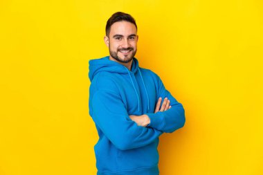 Sarı arka planda izole edilmiş, kolları çapraz ve ileriye bakan beyaz, yakışıklı genç bir adam.