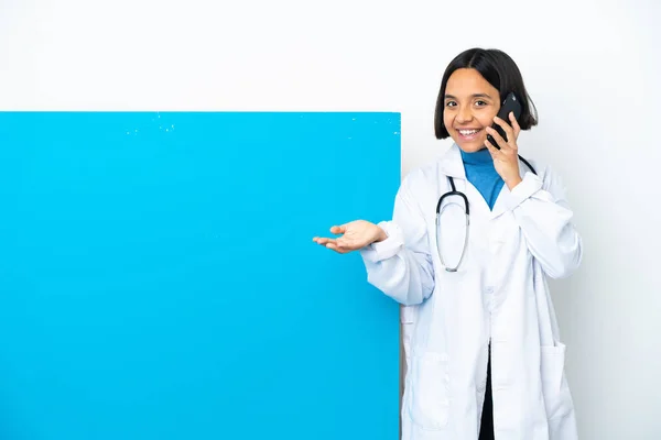 年轻的混合种族医生女人 有一个白色背景的大标语牌 和别人用手机交谈 — 图库照片