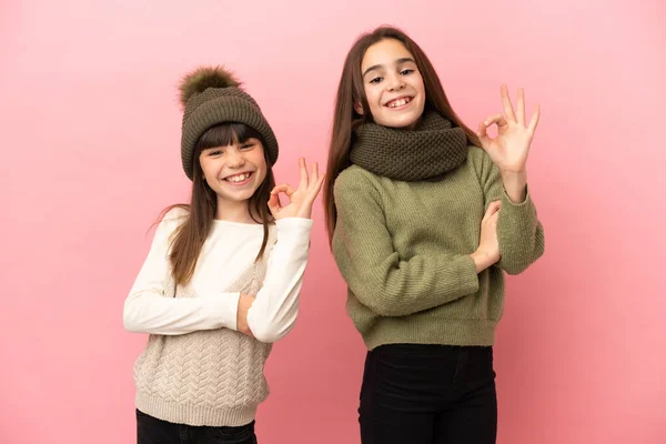 Hermanitas Vestidas Con Ropa Invierno Aisladas Sobre Fondo Rosa Mostrando —  Fotos de Stock