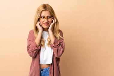 Genç Uruguaylı sarışın kadın, izole edilmiş arka planda hayal kırıklığına uğramış ve kulaklarını kapatmış.