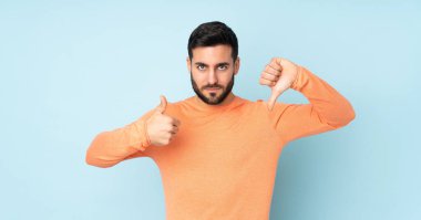 Kafkasyalı yakışıklı adam iyiye kötüye işaret veriyor. Evet ya da hayır arasında kararsız mavi arkaplan