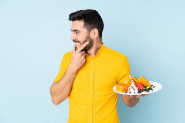 Mavi arka planda gözleme tutan beyaz bir adam bir fikir üretiyor ve ona bakıyor.