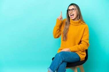 Mavi arka planda izole edilmiş bir sandalyede oturan beyaz bir kadın çözümün farkına varmak için parmağını kaldırıyor.