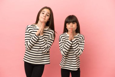 Pembe arka planda izole edilmiş küçük kız kardeşler avuç içlerini bir arada tutar. İnsan bir şey ister.