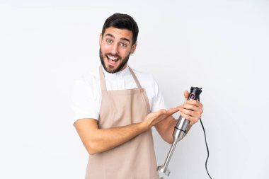 Beyaz arka planda izole edilmiş el blenderi kullanan adam davet edilmek için ellerini yana uzatıyor