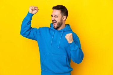 Sarı arka planda izole edilmiş beyaz yakışıklı bir adam zaferi kutluyor.