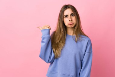 Soyutlanmış pembe arka planı olan genç bir kadın mutsuz ve bir tarafı işaret ediyor.