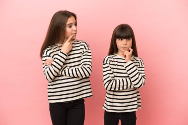 Pembe arka planda izole edilmiş küçük kız kardeşler yukarı bakarken şüphe duyarlar.