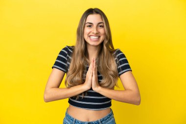 Sarı arka planda izole edilmiş genç beyaz kadın avuç içlerini bir arada tutuyor. İnsan bir şey ister.