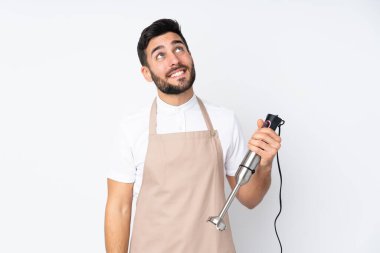 Beyaz arka planda izole edilmiş el blenderi kullanan adam gülüyor ve yukarı bakıyor.