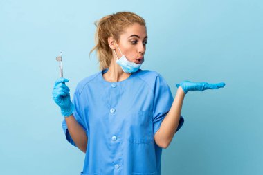 İzole edilmiş mavi arka plan üzerinde aletleri tutan genç bir dişçi.