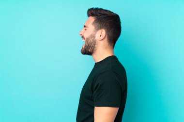 Beyaz tenli yakışıklı adam mavi arka planda izole edilmiş. Yan pozisyonda gülüyor.