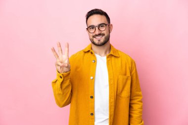 Beyaz tenli yakışıklı adam pembe arka planda izole edilmiş mutlu ve parmaklarıyla üçe kadar sayıyor.