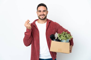 Beyaz arka planda izole edilmiş eşyalarla dolu bir kutuyu alıp para hareketi yapan genç beyaz bir adam.