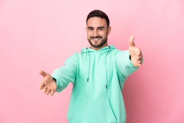 Beyaz tenli yakışıklı adam pembe arka planda izole edilmiş sunar ve davet edilir.