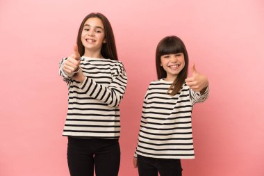 Küçük kız kardeşler pembe arka planda izole edilmiş güzel bir şey olduğu için iyi bir jest yapıyorlar.