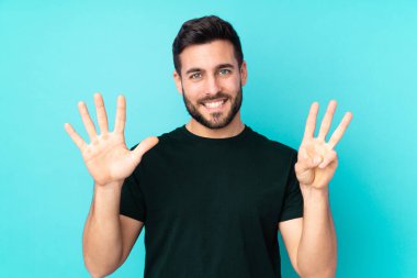 Beyaz tenli yakışıklı adam mavi arka planda izole edilmiş, parmaklarıyla sekizi sayıyor.