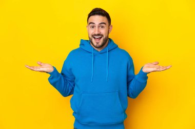 Sarı arka planda izole edilmiş, yüzü şoke olmuş, beyaz, yakışıklı genç bir adam.